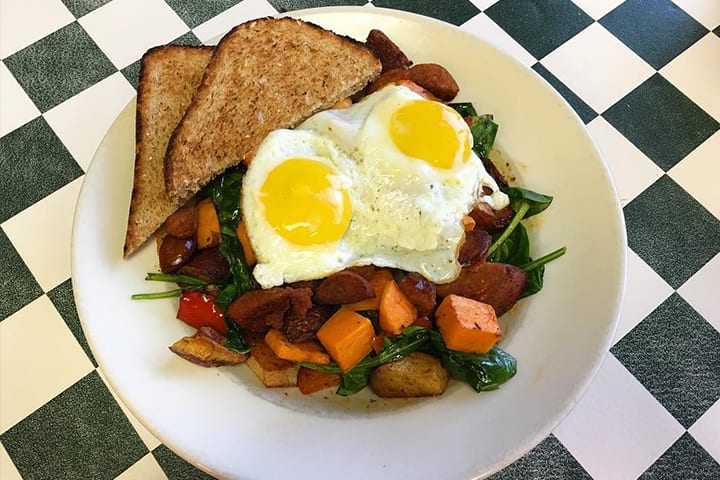 A breakfast bowl of grits topped with two eggs, melted cheese and sautéed vegetables.