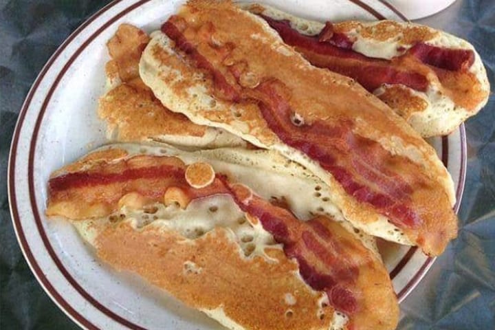 A plate sized pancake stuffed with bacon and sausage and topped with two eggs.