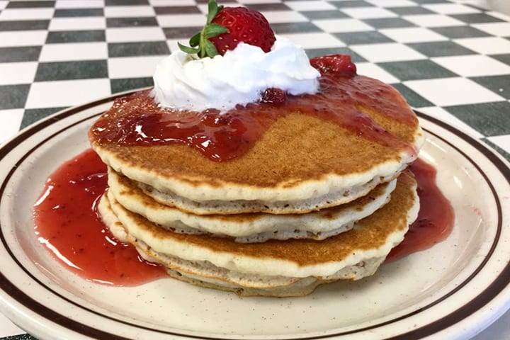 Pancakes topped with sliced strawberries and powdered sugar.
